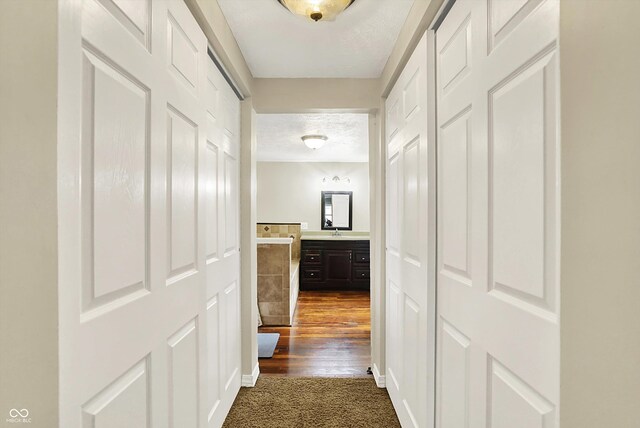 hallway featuring a textured ceiling, dark colored carpet, and baseboards