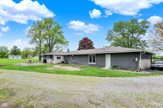back of house featuring a patio, brick siding, a lawn, and a chimney