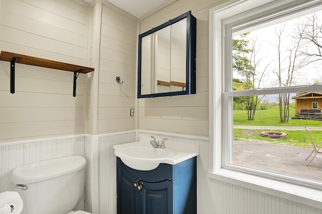 bathroom featuring toilet, vanity, a wainscoted wall, and wood walls