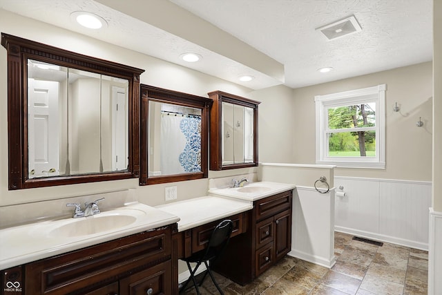 full bathroom with double vanity, wainscoting, a textured ceiling, and recessed lighting