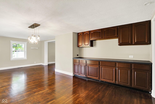 kitchen featuring a chandelier, dark wood-style flooring, baseboards, a textured ceiling, and decorative light fixtures