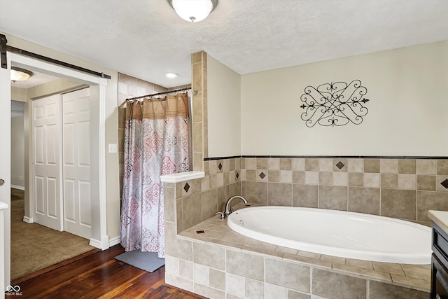 full bathroom with wood finished floors, a bath, tiled shower, a textured ceiling, and baseboards