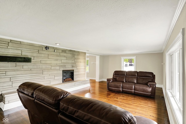 living room with crown molding, wood finished floors, a textured ceiling, baseboards, and a stone fireplace