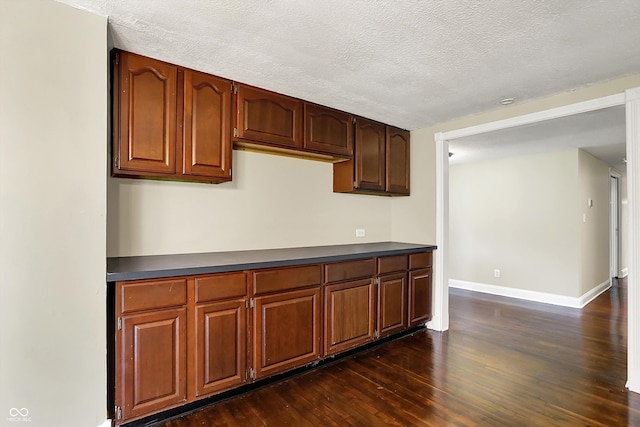 kitchen with dark wood-type flooring, dark countertops, baseboards, and a textured ceiling