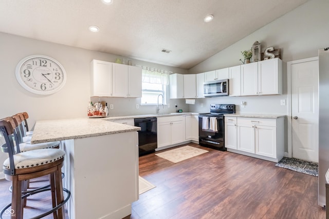 kitchen with a peninsula, white cabinetry, dark wood-type flooring, black appliances, and vaulted ceiling
