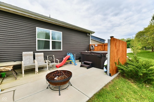 view of patio with fence, a hot tub, and a fire pit