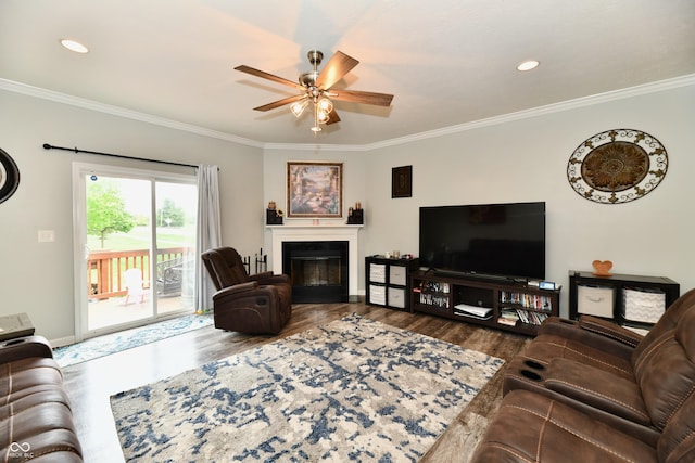 living room featuring ceiling fan, a glass covered fireplace, baseboards, wood finished floors, and ornamental molding