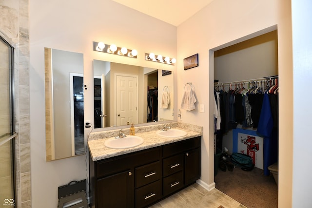 bathroom featuring double vanity, a sink, a walk in closet, and tiled shower