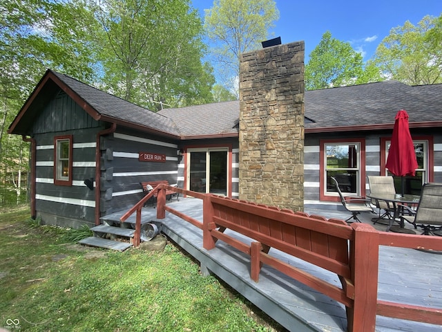 back of house featuring a chimney, roof with shingles, and a wooden deck