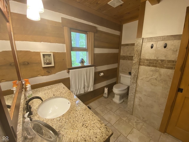 bathroom with vanity, toilet, wood walls, visible vents, and wood ceiling