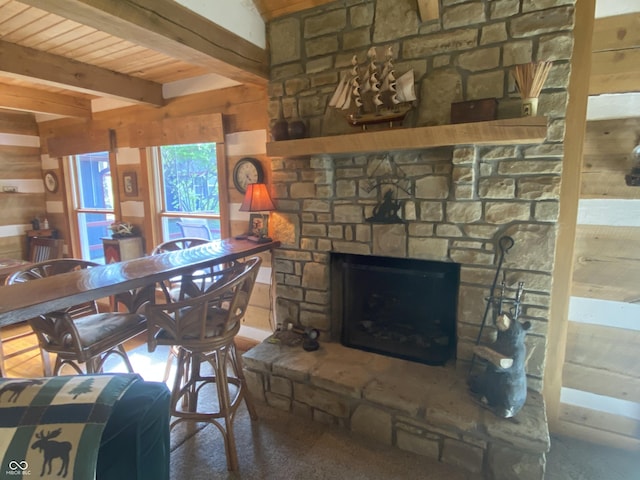 dining area featuring wooden ceiling, wood walls, a stone fireplace, and beam ceiling