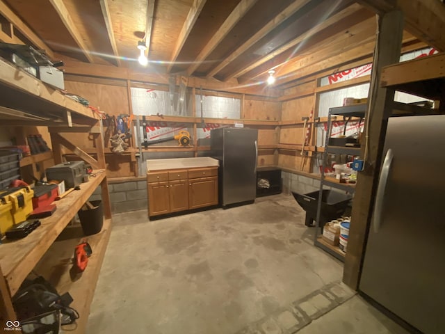 unfinished below grade area featuring freestanding refrigerator and a workshop area