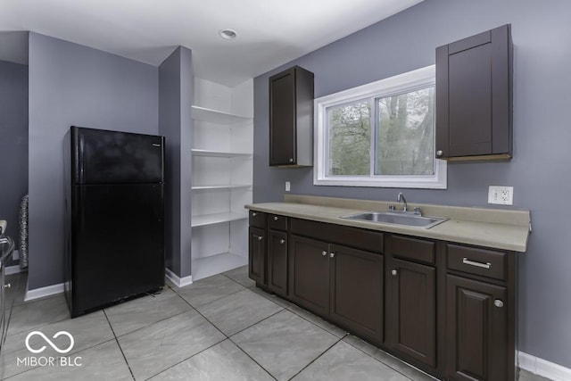 kitchen with open shelves, a sink, light countertops, freestanding refrigerator, and baseboards