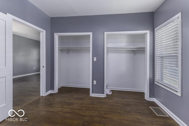 unfurnished bedroom featuring visible vents, baseboards, two closets, and wood finished floors