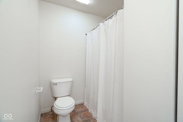 bathroom with baseboards, stone finish floor, toilet, and a shower with shower curtain