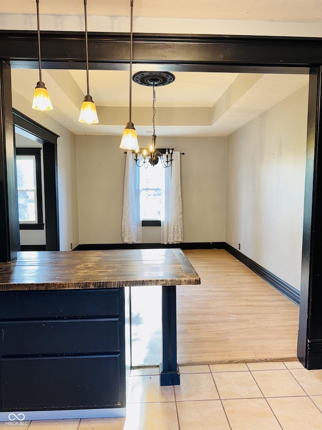 kitchen featuring an inviting chandelier, pendant lighting, butcher block counters, light tile patterned flooring, and a tray ceiling