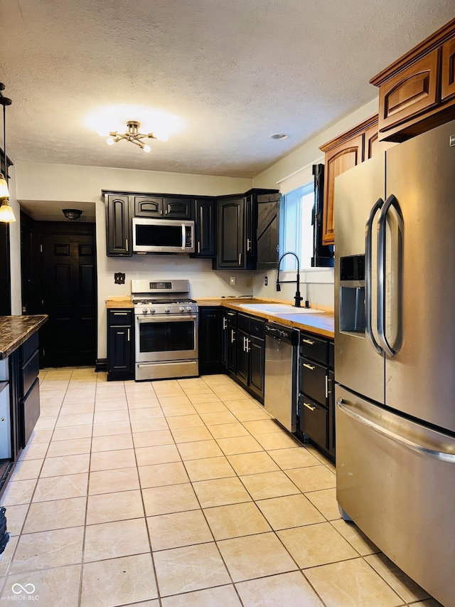 kitchen featuring a sink, appliances with stainless steel finishes, light tile patterned flooring, and a textured ceiling