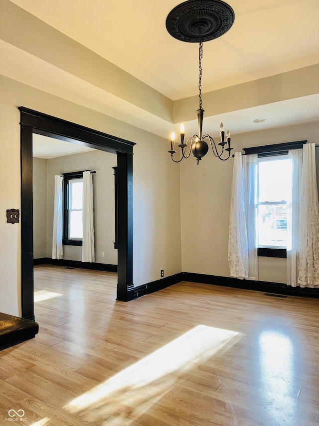 empty room featuring baseboards, light wood-style flooring, a notable chandelier, and visible vents