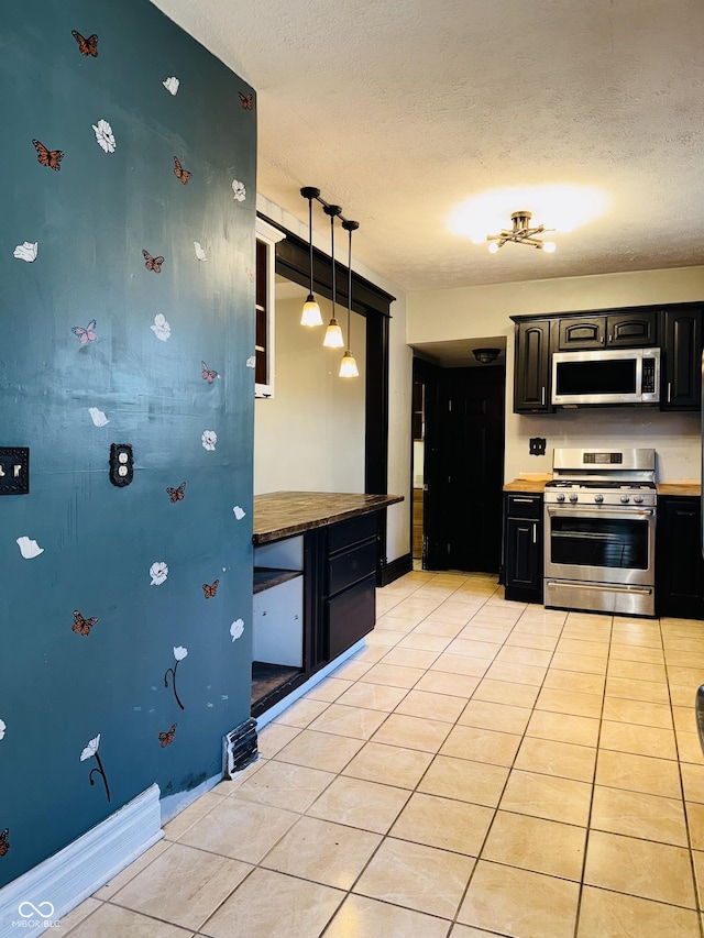 kitchen with hanging light fixtures, dark cabinets, a textured ceiling, stainless steel appliances, and light tile patterned floors