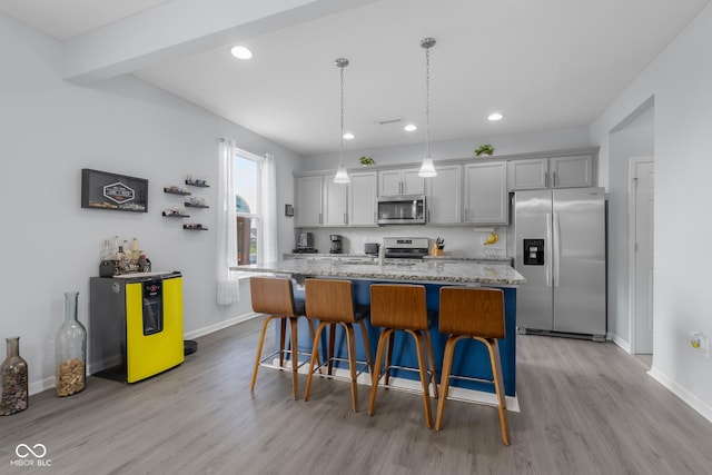 kitchen featuring light wood-style floors, a kitchen breakfast bar, an island with sink, stainless steel appliances, and baseboards