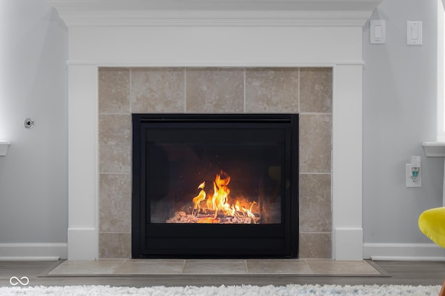 interior details featuring baseboards, a tiled fireplace, and wood finished floors