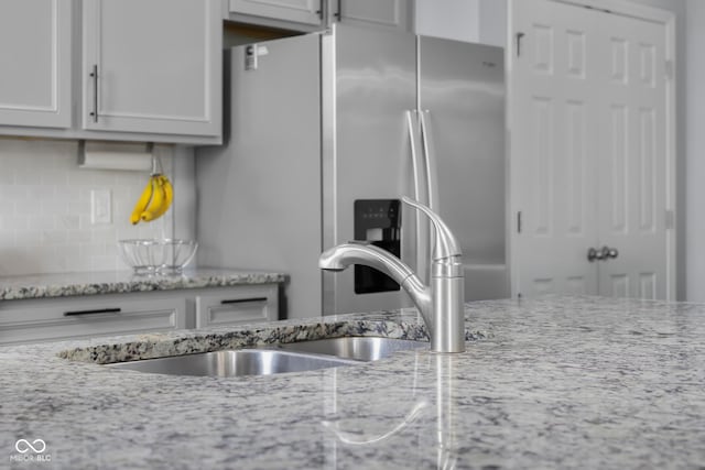 kitchen with a sink, stainless steel fridge with ice dispenser, tasteful backsplash, and light stone countertops