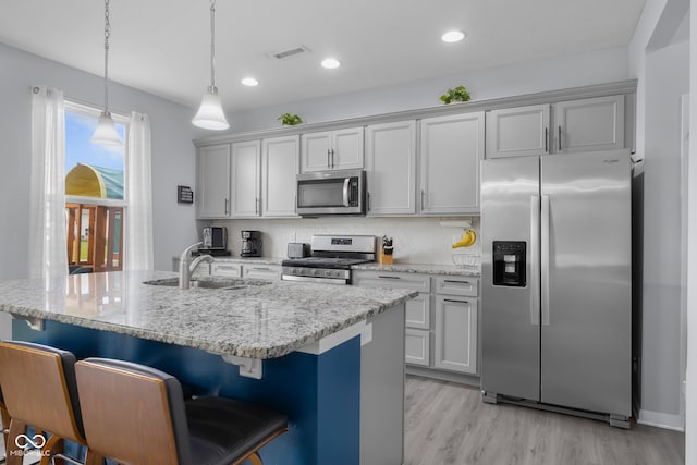 kitchen with a sink, light wood-style flooring, stainless steel appliances, a kitchen bar, and visible vents