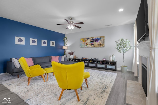 living area featuring a ceiling fan, baseboards, a fireplace with flush hearth, recessed lighting, and wood finished floors