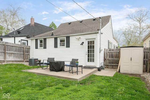 rear view of property with cooling unit, a fenced backyard, a storage unit, a patio area, and a lawn
