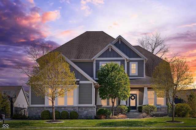craftsman-style home with board and batten siding, stone siding, a front yard, a porch, and a shingled roof