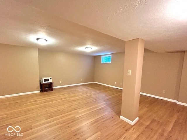 basement featuring baseboards, light wood finished floors, and a textured ceiling