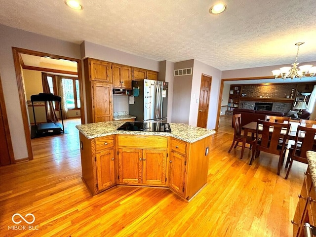 kitchen featuring brown cabinetry, visible vents, black electric cooktop, freestanding refrigerator, and light wood-style floors