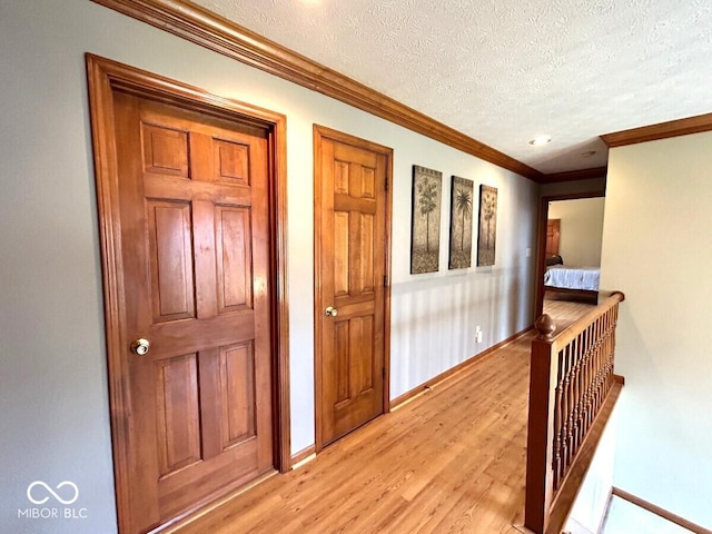 corridor with light wood-style floors, a textured ceiling, baseboards, and crown molding