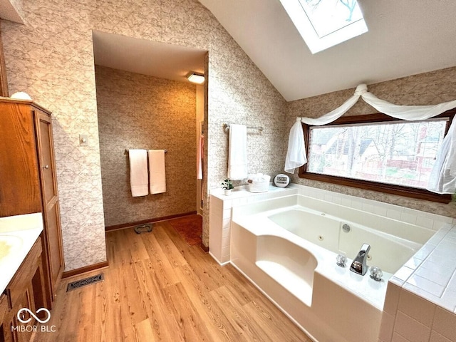 full bath with visible vents, vanity, wood finished floors, a jetted tub, and lofted ceiling with skylight