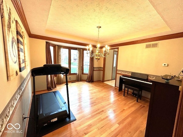 exercise room featuring a raised ceiling, a notable chandelier, a textured ceiling, and visible vents