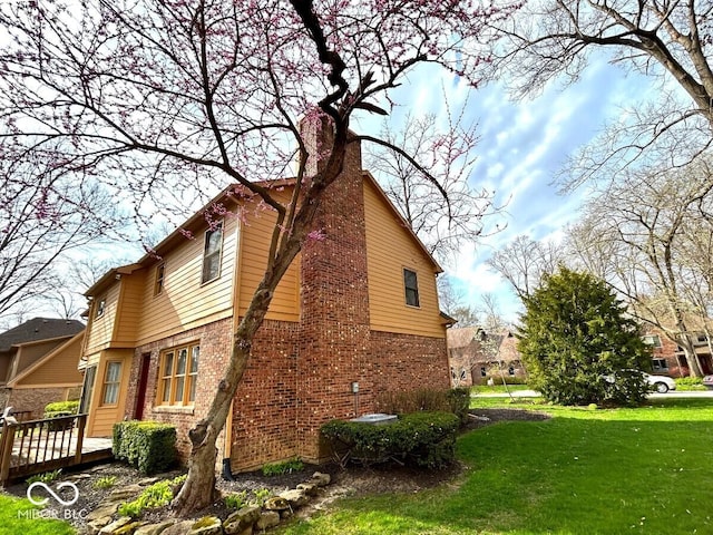 view of home's exterior featuring a lawn, brick siding, a chimney, and a wooden deck