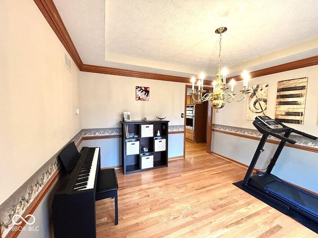 workout area with an inviting chandelier, visible vents, wood finished floors, a raised ceiling, and a textured ceiling