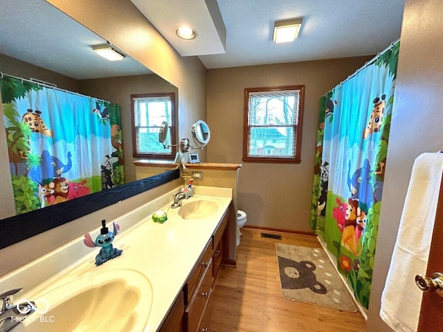 full bath featuring toilet, a wealth of natural light, a sink, and wood finished floors