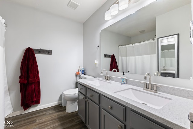 bathroom with a sink, toilet, wood finished floors, and visible vents