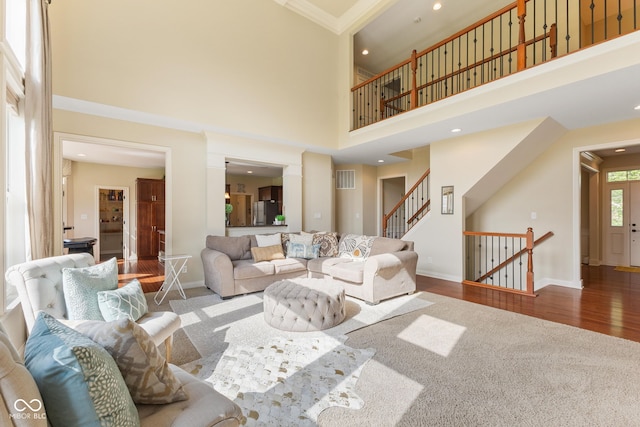 living area with a high ceiling, baseboards, visible vents, ornamental molding, and stairway
