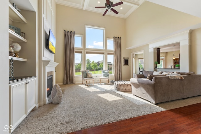 living area featuring a wealth of natural light, ceiling fan, a lit fireplace, and a towering ceiling