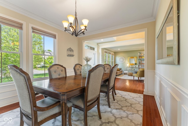 dining space with crown molding, wainscoting, a decorative wall, a chandelier, and wood finished floors