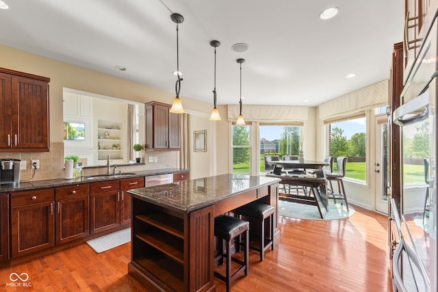 kitchen featuring stainless steel dishwasher, open shelves, a kitchen island, a breakfast bar, and a sink