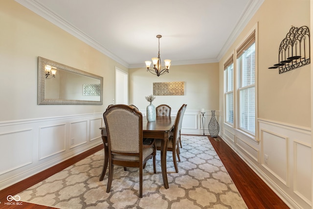 dining room featuring crown molding, a notable chandelier, wood finished floors, and a decorative wall