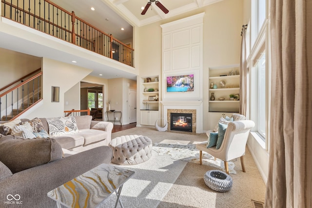 living room with crown molding, stairs, a glass covered fireplace, a high ceiling, and a ceiling fan