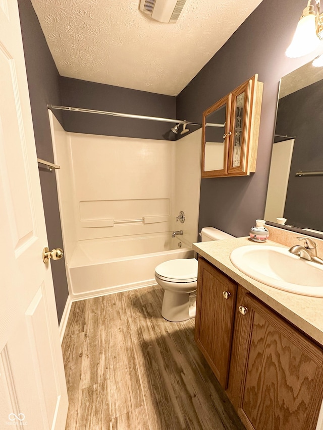 bathroom with toilet, a textured ceiling, wood finished floors,  shower combination, and visible vents
