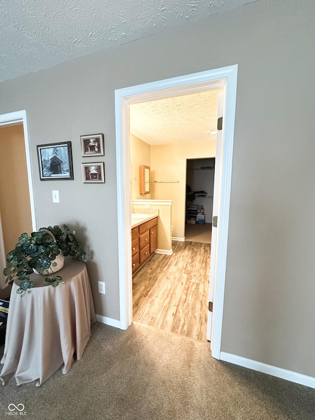 corridor featuring baseboards, a textured ceiling, and light colored carpet