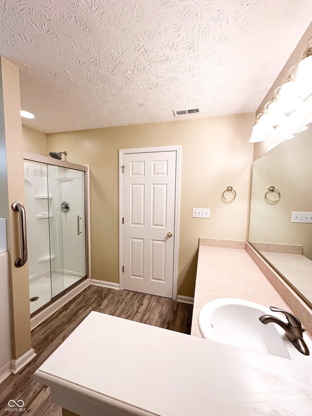 bathroom featuring visible vents, wood finished floors, baseboards, a textured ceiling, and a shower stall