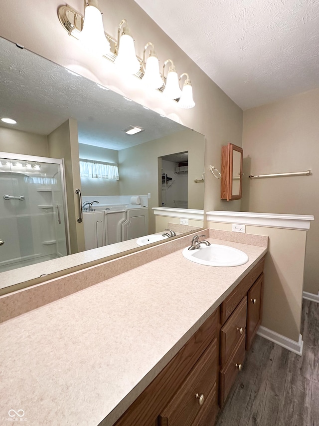 full bath featuring a textured ceiling, wood finished floors, vanity, baseboards, and a shower with door