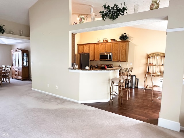 kitchen featuring baseboards, appliances with stainless steel finishes, brown cabinetry, and dark colored carpet
